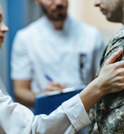 Close-up of a soldier being consoled by healthcare workers at clinic.