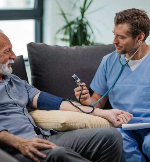 Happy general practitioner measuring blood pressure of mature man while being in a home visit.